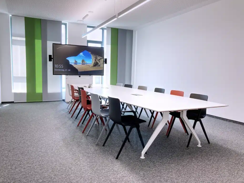 AOK großer Besprechungsraum Großer Besprechungsraum mit langem Tisch und 12 Stühlen sowie großem Bildschirm auf einer Videokonferenzstele - AOK Nürnberg