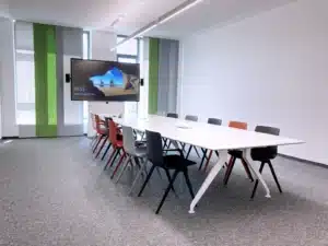 Großer Besprechungsraum mit langem Tisch und 12 Stühlen sowie großem Bildschirm auf einer Videokonferenzstele - AOK Nürnberg