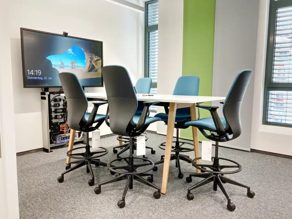 AOK-Stehtisch Seminarraum mit Stehtisch und großem Display mit Kamera auf einer offenen Videokonferenzstele, wo die Steuerungstechnik zu sehen ist, bei der AOK Nürnberg